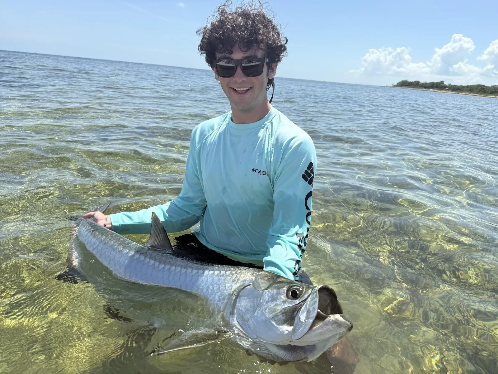 Angler kneeling in shallow water with a tarpon on the flats
